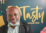 Image of Michael Olaleye, founder and managing director of Tasty African Food, in front of a blurred sign reading Tasty African Food