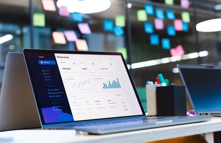 CRM software is displayed on a laptop in front of a wall of sticky notes