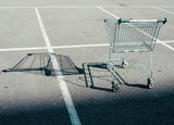 An empty shopping cart casts a shadow over an empty car park