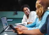A smiling woman talks to her colleague in front of a laptop