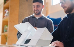 Two men standing behind and using a white POS system, including a white terminal and printer
