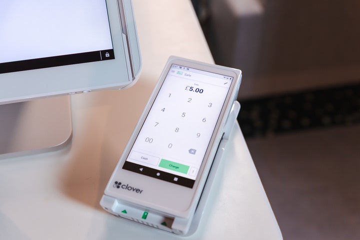 I white Clover Flex card reader with illuminated display lying on a white surface next to a monitor