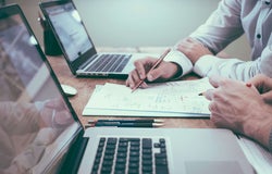 Two colleagues complete paperwork in front of their laptops