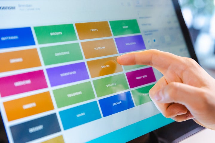 A close-up of the Epos Now POS terminal, with a finger touching the screen that shows a variety of categories in a range of colours