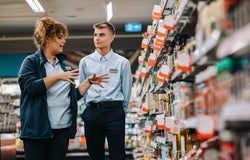 A store supervisor giving training to an employee in the middle of a supermarket aisle.