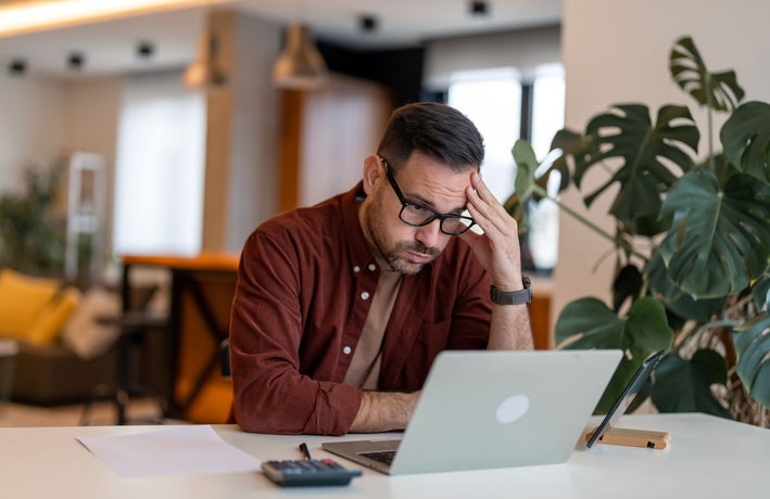 Contemplating businessman in the home office feeling frustrated. Full concentration on work. Man working on laptop, counting profit while sitting at the desk at home.