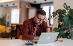 Contemplating businessman in the home office feeling frustrated. Full concentration on work. Man working on laptop, counting profit while sitting at the desk at home.