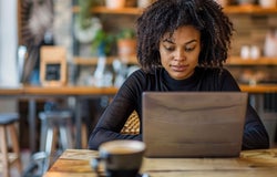 A woman with a black sweater sitting at wooden cafe table with a brown laptop.