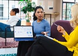 A woman shows her laptop screen to a colleague during a meeting