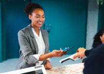 A smiling woman taps her smartphone on a payment terminal