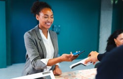A smiling woman taps her smartphone on a payment terminal