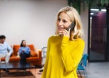 Woman standing in an office using her personal phone to make a call while colleagues work behind her