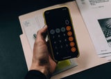 A hand holds a smartphone with a the calculator app open.