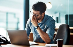 An exasperated man sits in front of his work laptop